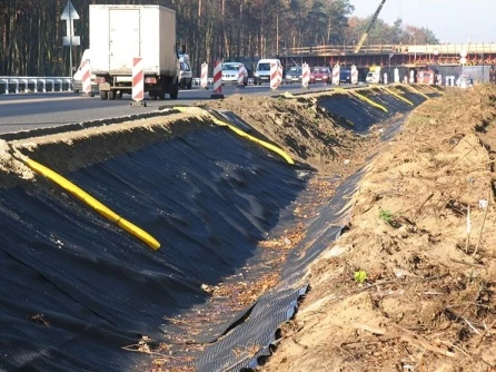 Instalace nopové folie na svahu vedle silnice s žlutými hranami.