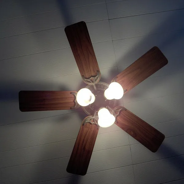 Stropní ventilátor s dřevěnými lopatkami a zapnutými světly.