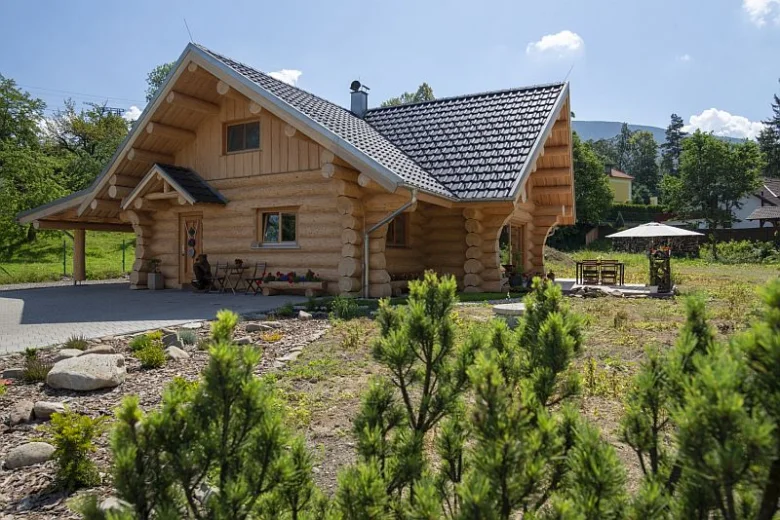 Tradiční dřevěný srub stojí na trávníku pod modrou oblohou.