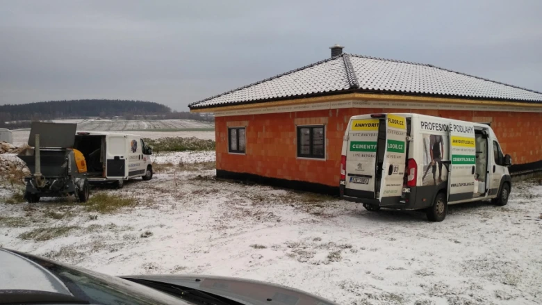 Stavba domu s betonovou podlahou v zimě a nájezdová vozidla.
