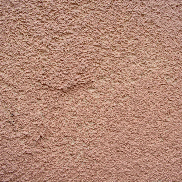 Detail škrábané omítky na zdi s viditelnými drasami.