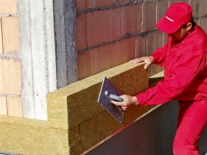 Stavebník aplikuje žlutou tepelněizolační desku na cihlový zdivo.