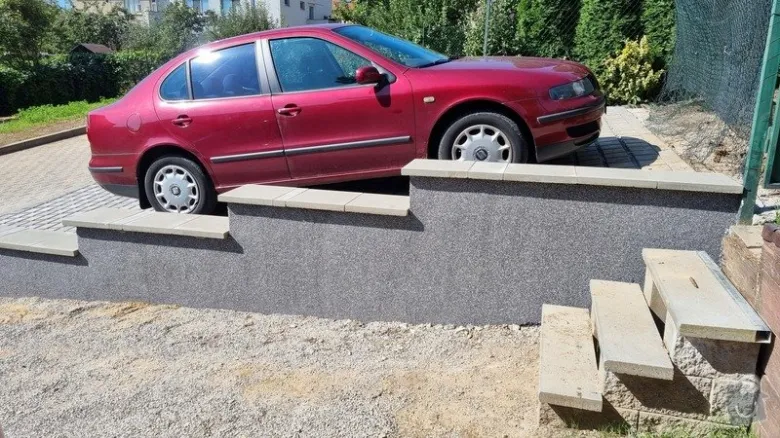 Červené auto na betonovém vjezdu do garáže s kamennými schody.