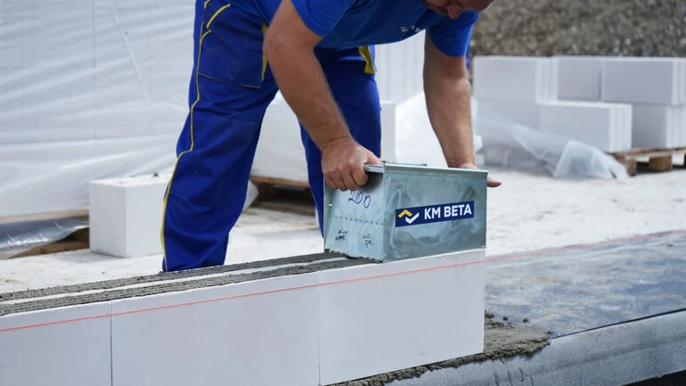 Stavebník nanáší maltu na betonový blok při stavbě zdi.