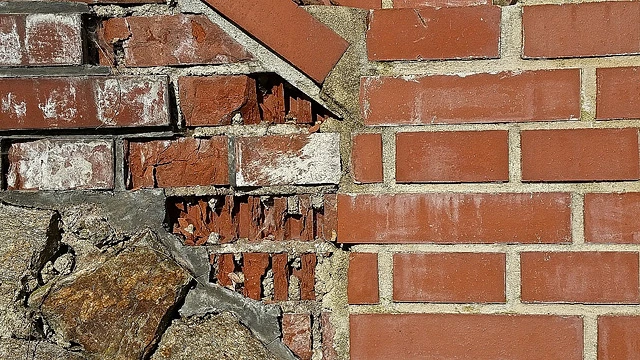 Poškozená cihlová zeď s odhalenou maltou a kamenem podkladu