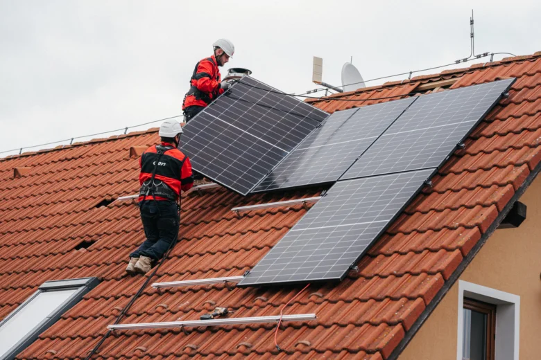 Dva pracovníci montují fotovoltaické panely na střechu.