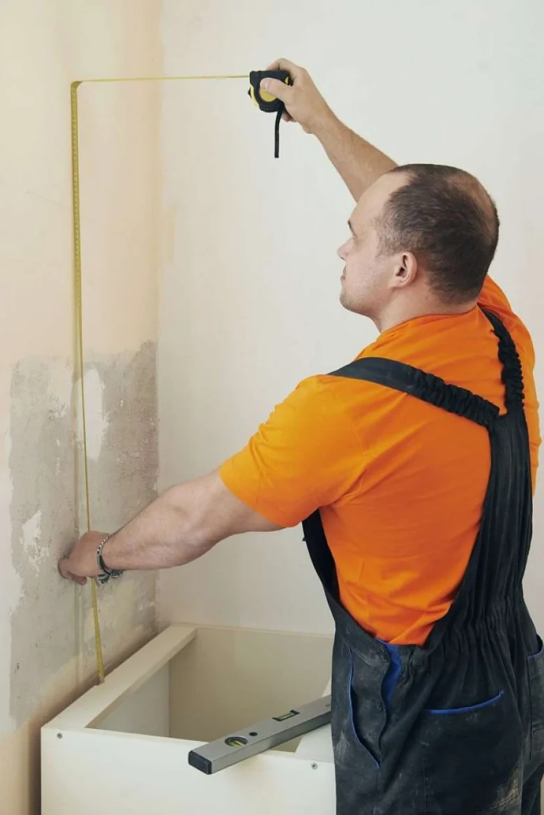 Muž měří výšku stěny pro instalaci horních skříní kuchyně.