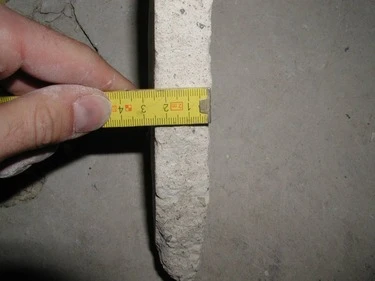 Měření tloušťky betonového potěru páskou na stavebním pruhu.