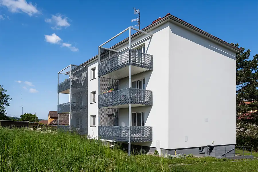 Moderní balkony s kovovými mřížemi na rekonstruovaném bytovém domě.