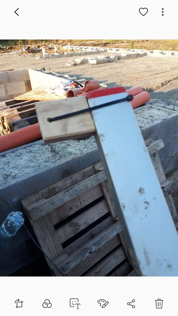 Dřevěné bednění pro betonování základů s cihlovou zdí na pozadí.