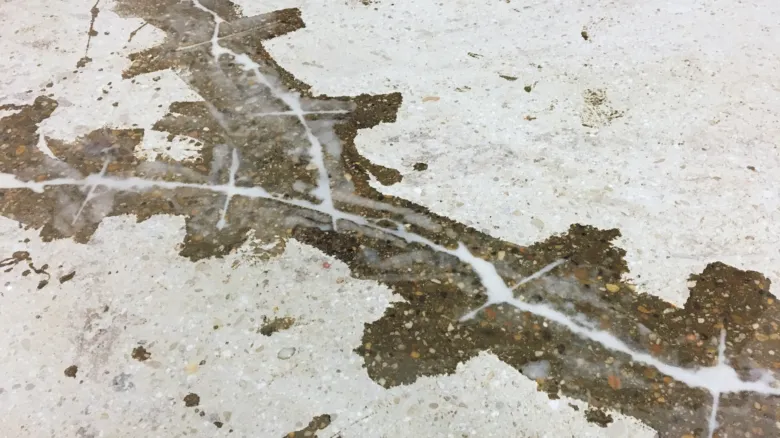 Poškozená betonová podlaha s prasklinami potřebující vyrovnání.