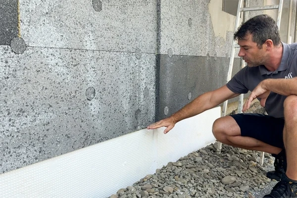 Muž instaluje bílou nopovou folii podél betonové zdi.