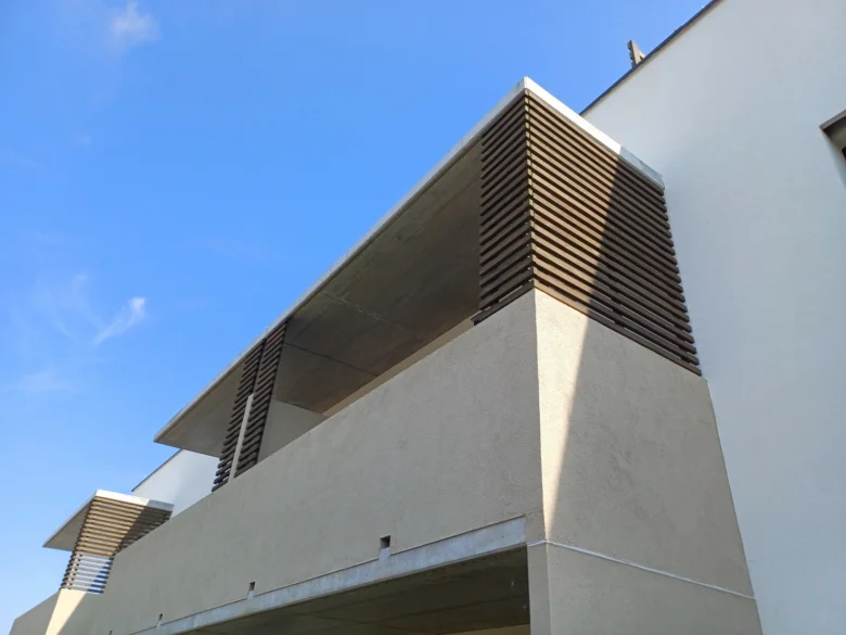 Detail dřevěných lamel na fasádě budovy pod betonovým přepadem.