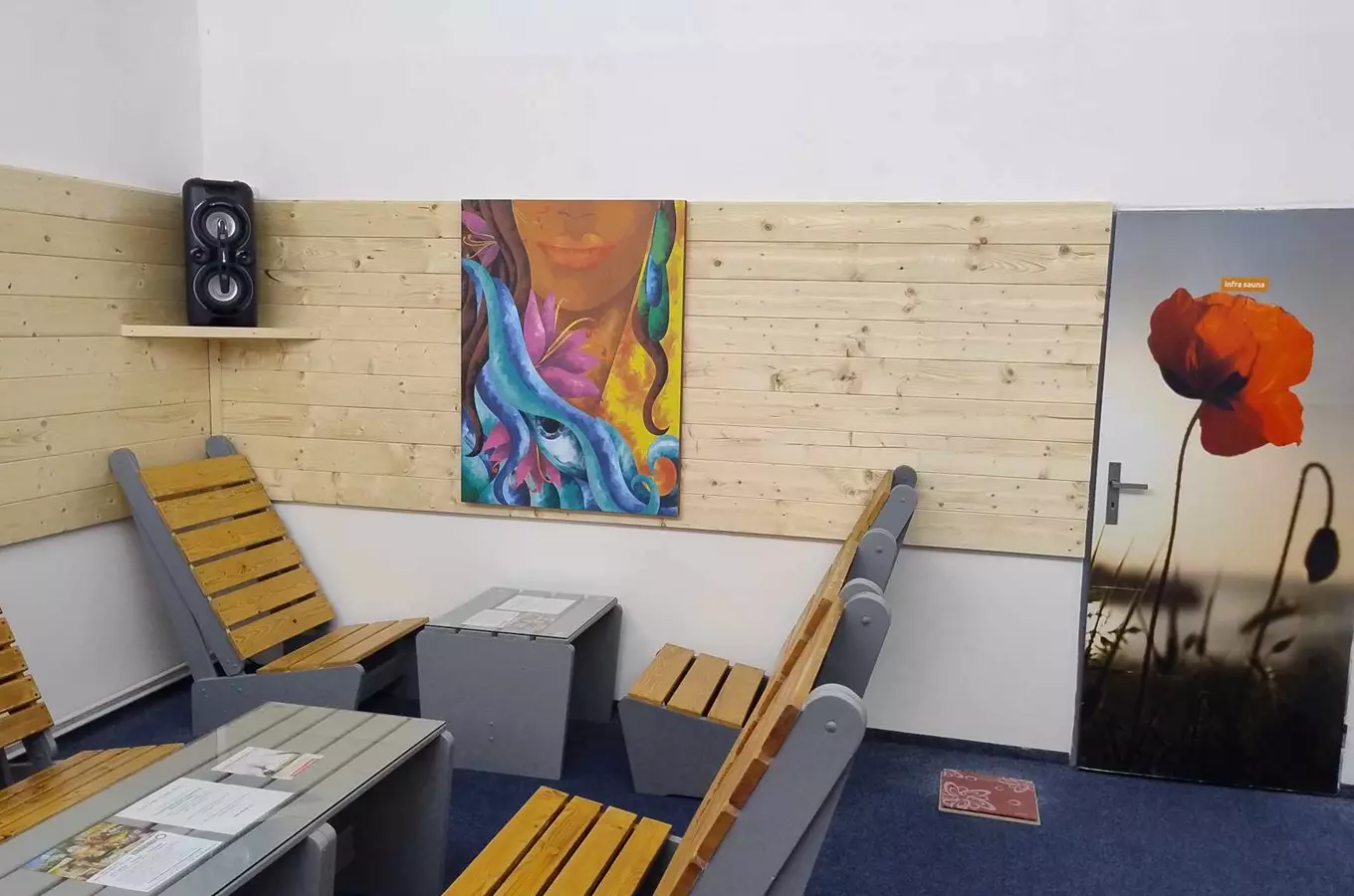 Vnitřek sauny s dřevěnými lavicemi a barevnou uměleckou výzdobou.