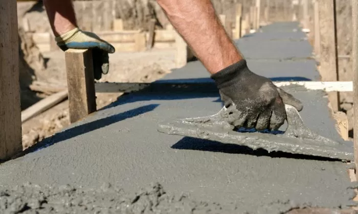 Stavebník hladí čerstvý beton na základě rukama.