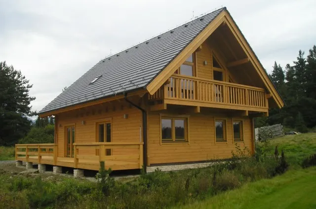 Dvoupatrová dřevěná chata s balkonem v přírodě.