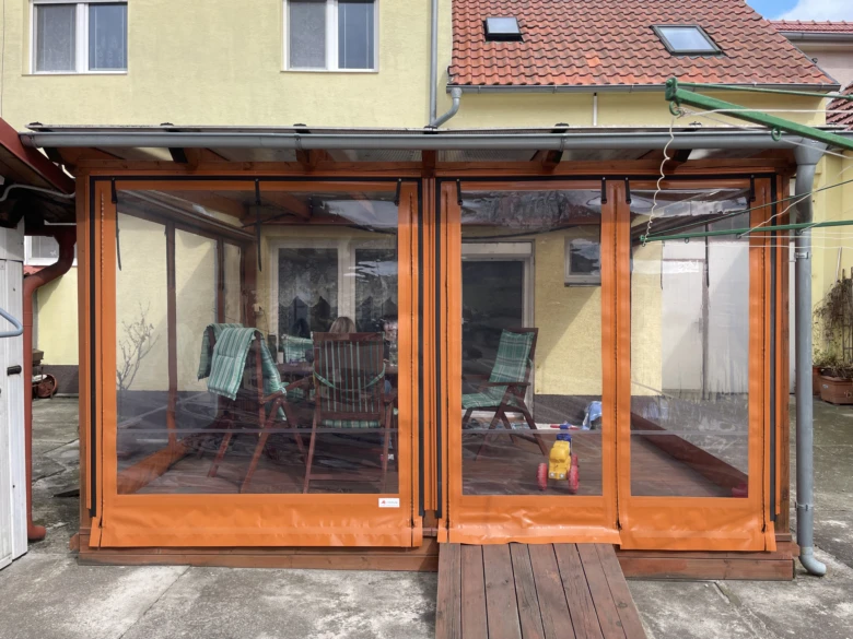 Oranžová plachta na dřevěné pergole v zahradním prostředí.