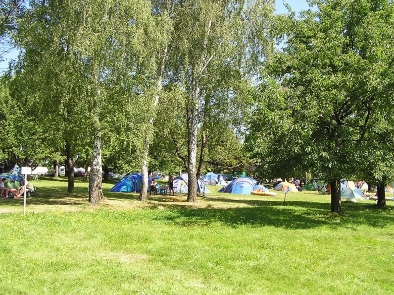 Kemp Olešná: barevné stany na trávníku mezi stromy.