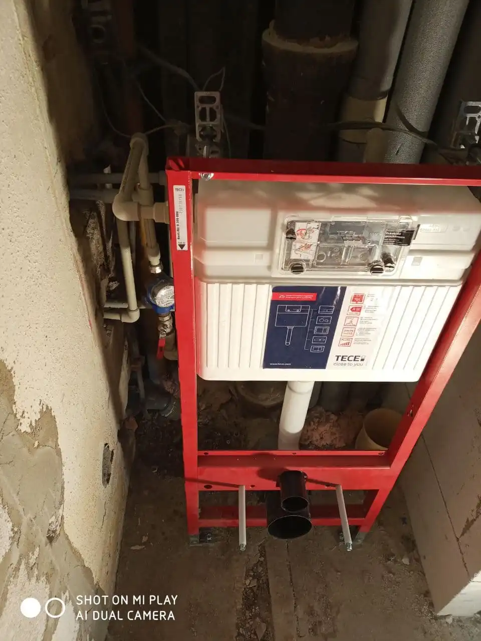 Rám pro instalaci záchodu s viditelnými potrubími a ventily.