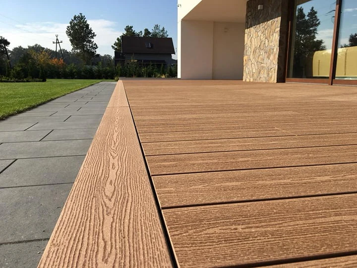 Moderní dřevěná terasa z kompozitových prken vedle dlažby.