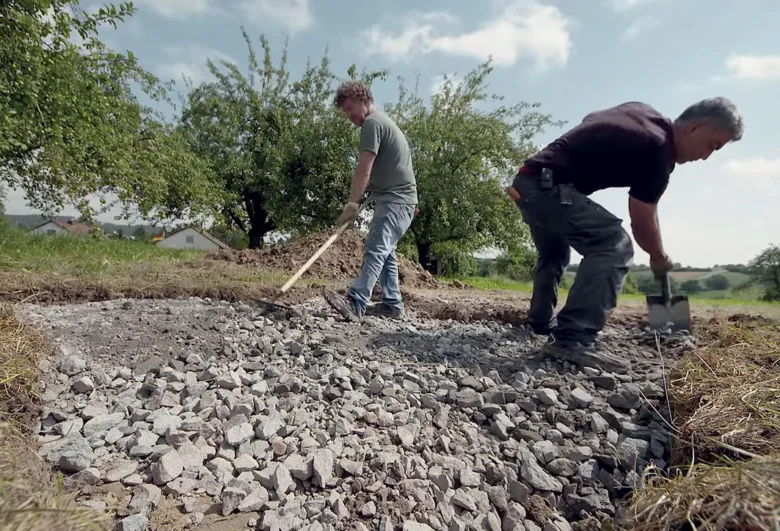 Muži připravují základovou plochu štěrkem před betonováním.
