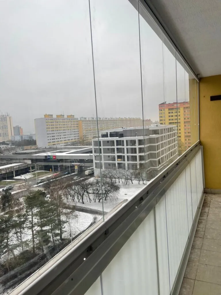 Zasklený balkon s výhledem na zasněženou ulici.