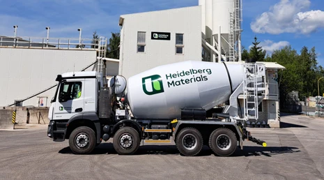 Bílý betonový smíchávač značky Heidelberg Materials na průmyslovém dvoře.