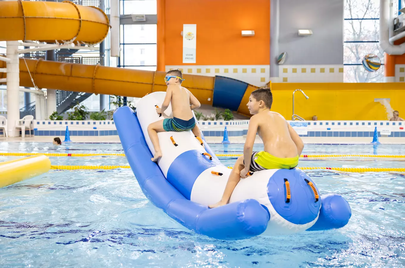 Dva chlapci na nafukovacím člunu v krytém bazénu.