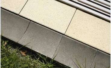 Betonové dlaždice na terase vedle trávníku s tmavým lemem.