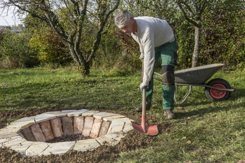 Muž staví kamenné ohniště z cihel a kamenů venku.