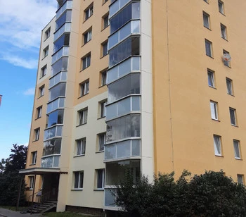 Panelový dům s zasklenými lodžiemi pod modrou oblohou.