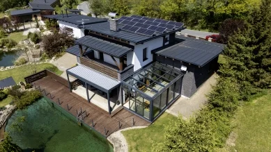 Modern dům s připojenou zimní zahradou na pozadí zelené zahrady.