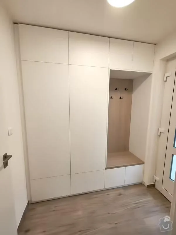 Bílá vestavěná skříň s úložným prostorem a sedacím místem.