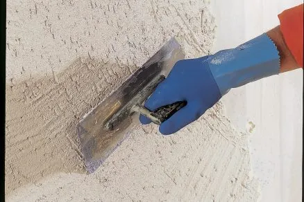 Ruční aplikace nové omítky na fasádu pomocí stěrky.