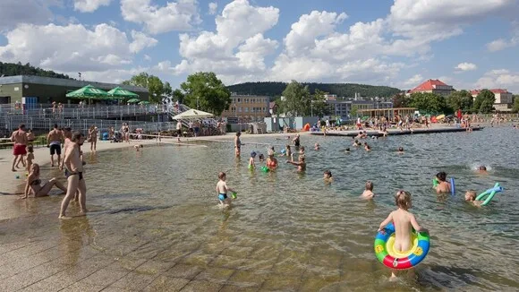 Lidé plavou a koupejí se v přírodním koupališti u budov.