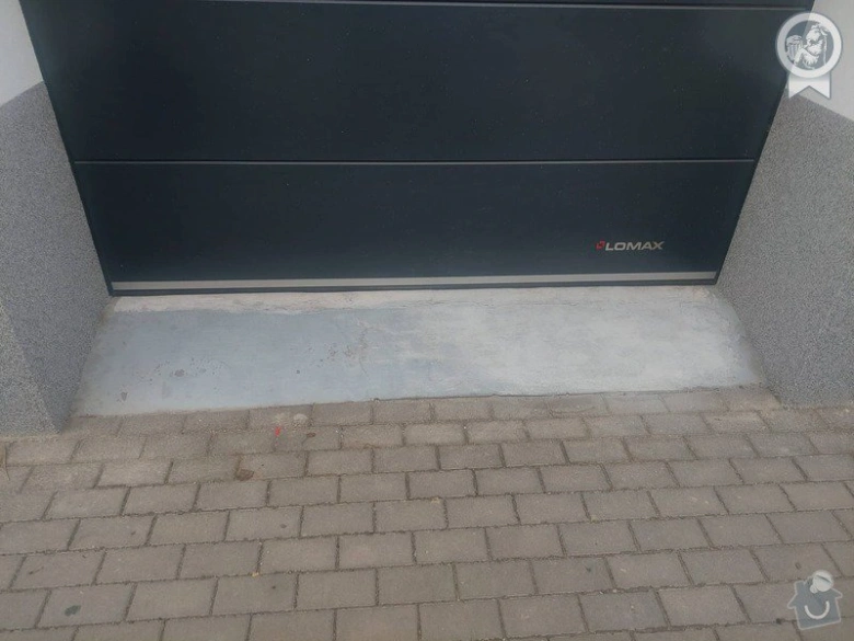 Vjezd do garáže s betonovým nájezdem před černou bránou.