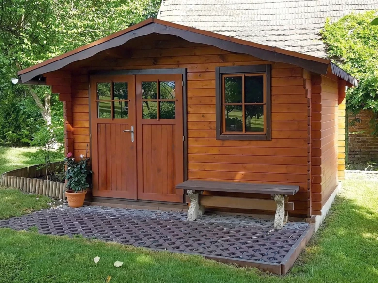 Dřevěný zahradní domek s lavičkou na kamenné terase.