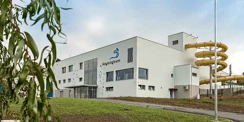 Bílá budova Aquacentrum s žlutými vodními skluzavkami venku.