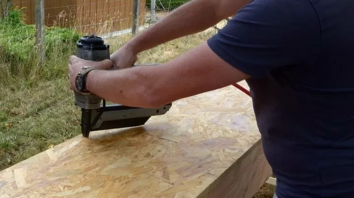 Muž používá dělníkový nůh na dřevěné desky venku.