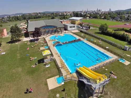 Vzdušný pohled na venkovní bazénový komplex s vodními skluzavkami a soláry.