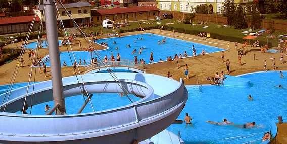 Venkovní bazén v Kopřivnici s tobogány a lidmi koupející se.