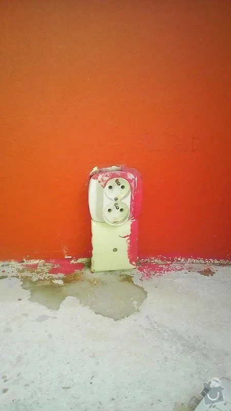 Poškozená elektrická zásuvka s odlupující se barvou a vodou na podlaze.