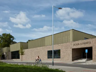 Exteriér bazénu Aquav Parku v Kyjově s cyklisty před budovou.