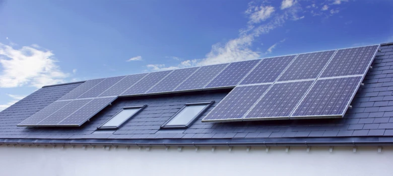 Fotovoltaické panely na střeše domu pod modrou oblohou.