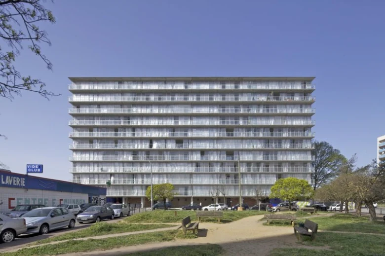 Velká betonová panelová budova s balkóny v městském prostředí.