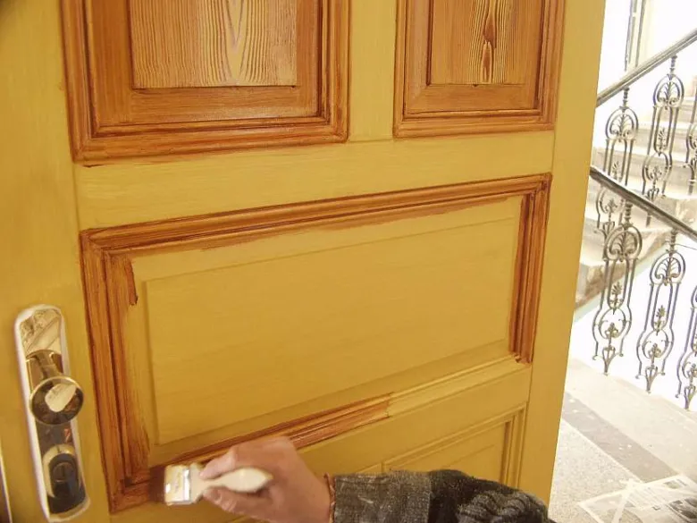 Ruční malování žlutou barvou na dřevěné dveře štětcem.