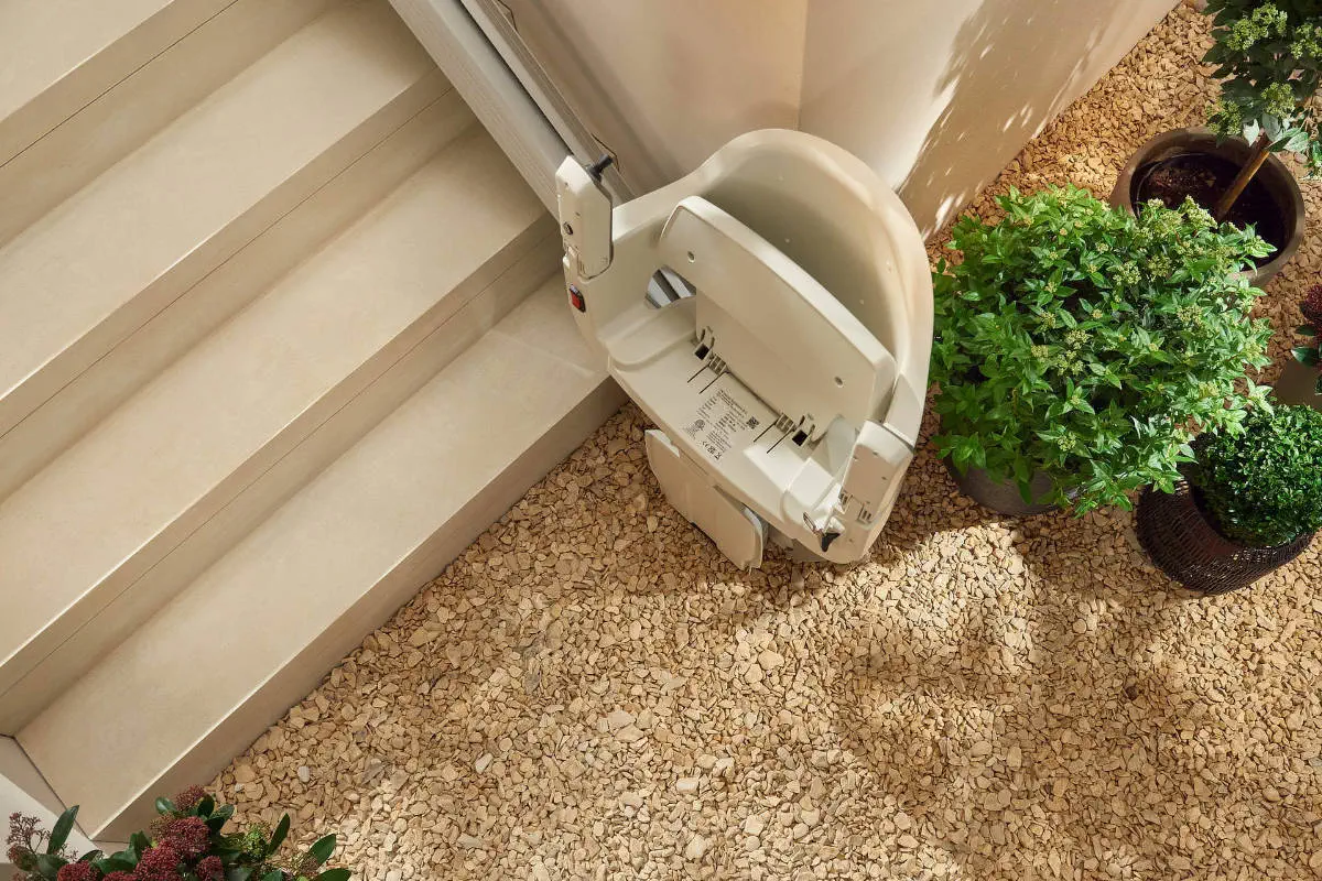 Stairlift na schodech vedle květin v zahradním prostředí.