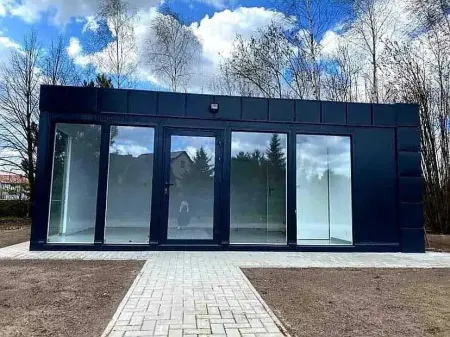 Moderní modrý kontejnerový dům s velkými okny na pozadí stromů.