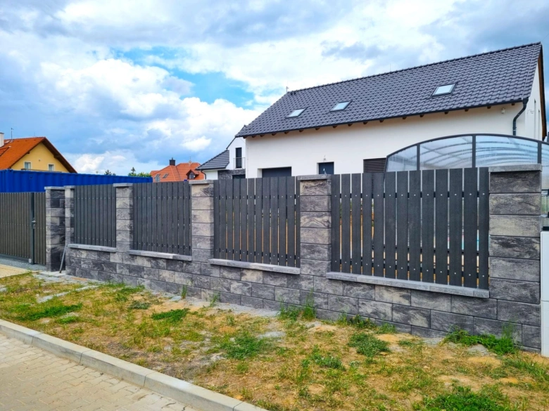 Neprůhledný zahradní plot s kamenným základem a tmavými lamelami.